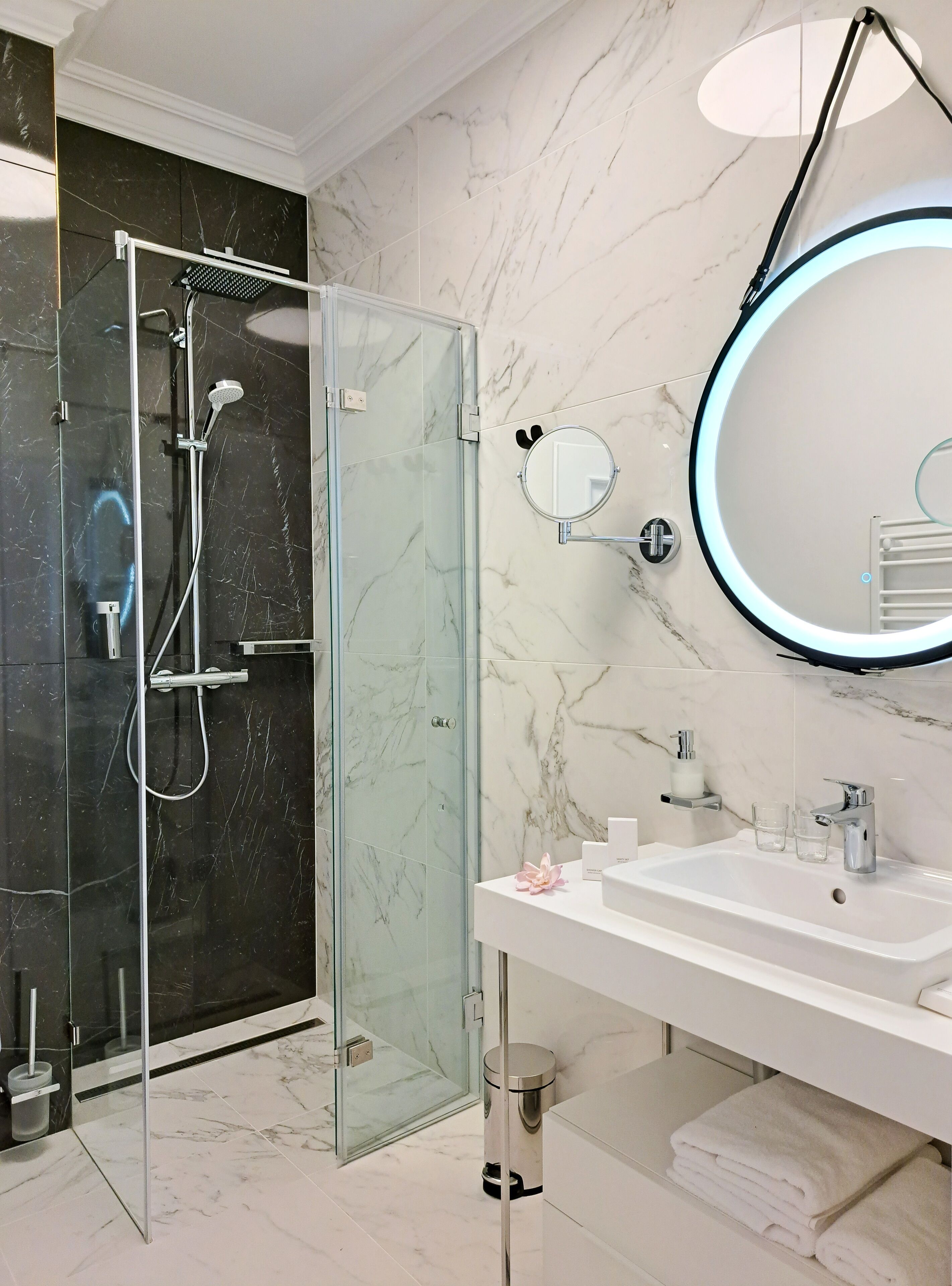 A modern bathroom with a glass-enclosed shower, a white sink with a mirror, and marble walls.