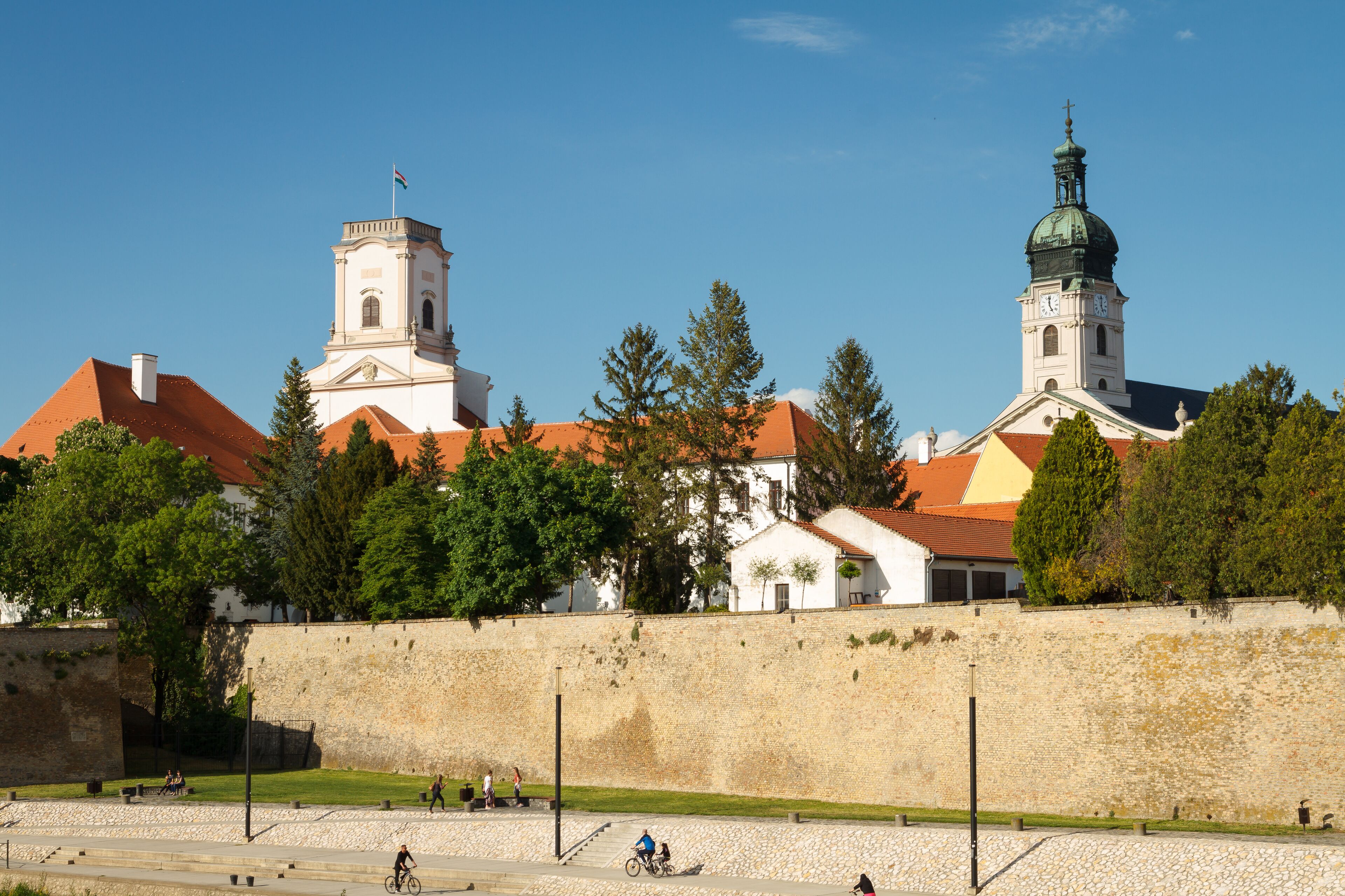 A historic building with a prominent tower and a dome, surrounded by a stone wall and greenery.