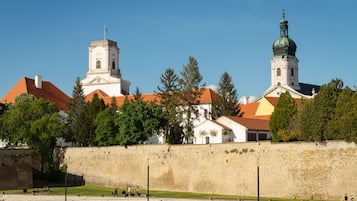 A historic building with a prominent tower and a dome, surrounded by a stone wall and greenery.