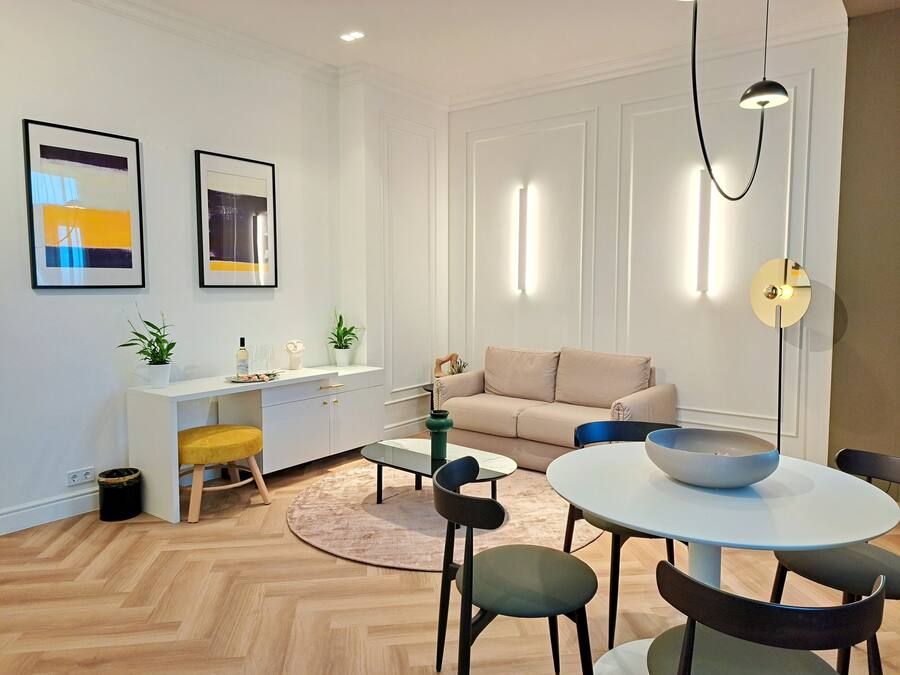 Una sala de estar moderna con un sofá, una mesa de comedor con sillas, una consola blanca con adornos y dos cuadros en la pared.