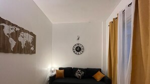 A living room with a black sofa, a small black table, a world map on the wall, a clock, and curtains. - Paris Appartement Centré Pour 4 (Paris)
