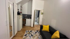 A modern apartment with a living area featuring a black sofa with yellow cushions, a geometric patterned rug, and a kitchen in the background. - Paris Appartement Centré Pour 4 (Paris)