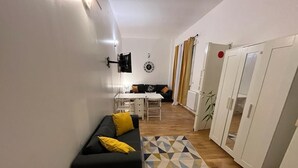 A compact living space with a black sofa, a patterned rug, a dining table, and a kitchen area. - Paris Appartement Centré Pour 4 (Paris)