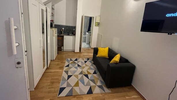 A modern living room with a black sofa, a geometric rug, and a flat-screen TV mounted on the wall. - Paris Appartement Centré Pour 4 (Paris)