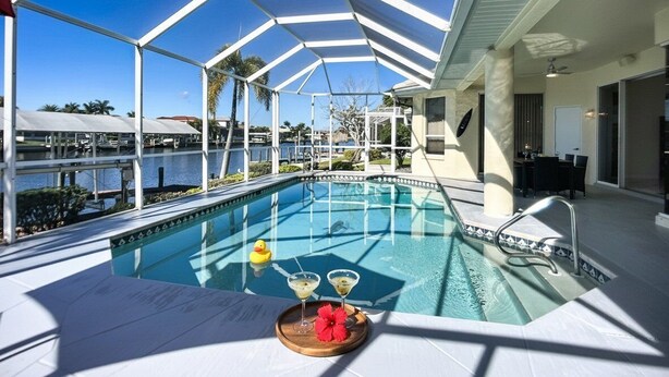 Piscina interna com vista desobstruída para os arredores, incluindo área ao lado da piscina com mesa e cadeiras, e vista para a massa d'água lá fora.