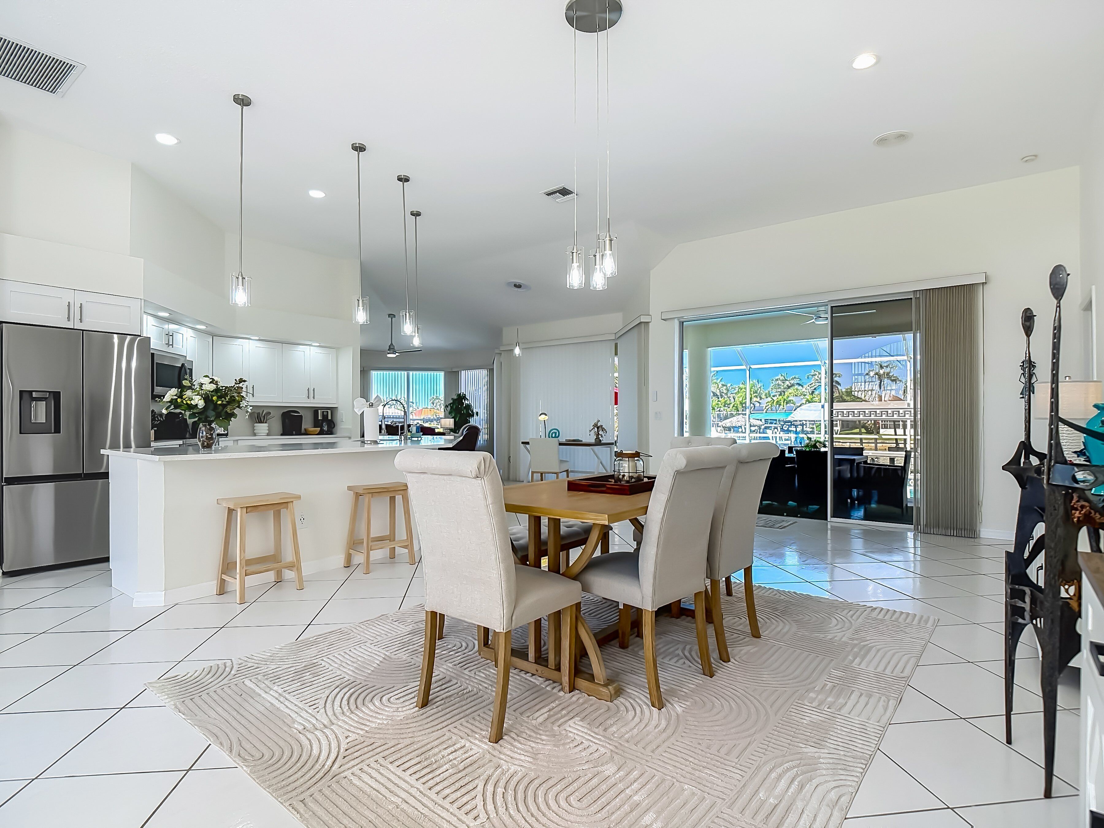 A modern kitchen with a central island, dining area with chairs, and a view through large windows.