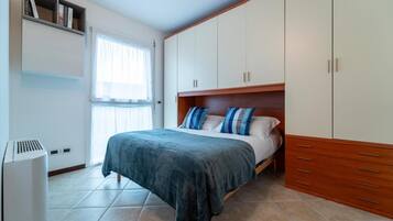 Un dormitorio con una cama, un armario, una estantería con libros y una ventana.