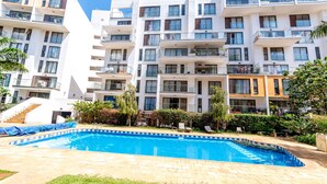 Un edificio de apartamentos moderno con piscina, balcones y zonas de estar al aire libre.