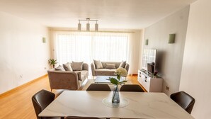Un comedor con una mesa de mármol, cuatro sillas, un jarrón con flores y un sofá al fondo.