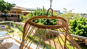 Una silla colgante de mimbre con cojines en un balcón con vistas a un jardín y una piscina.