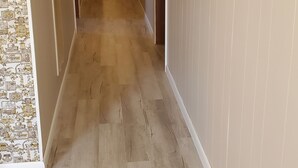 Un lungo e stretto corridoio con pavimento in legno e pareti dai toni chiari.