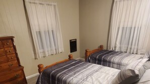 Una camera da letto con due letti, testiere in legno, una cassettiera e una finestra con tende leggere.
