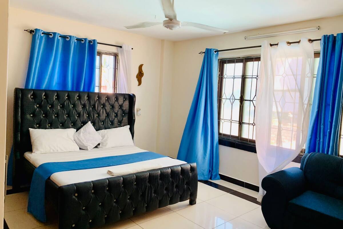 A bedroom with a large bed, a ceiling fan, and a window with blue curtains.