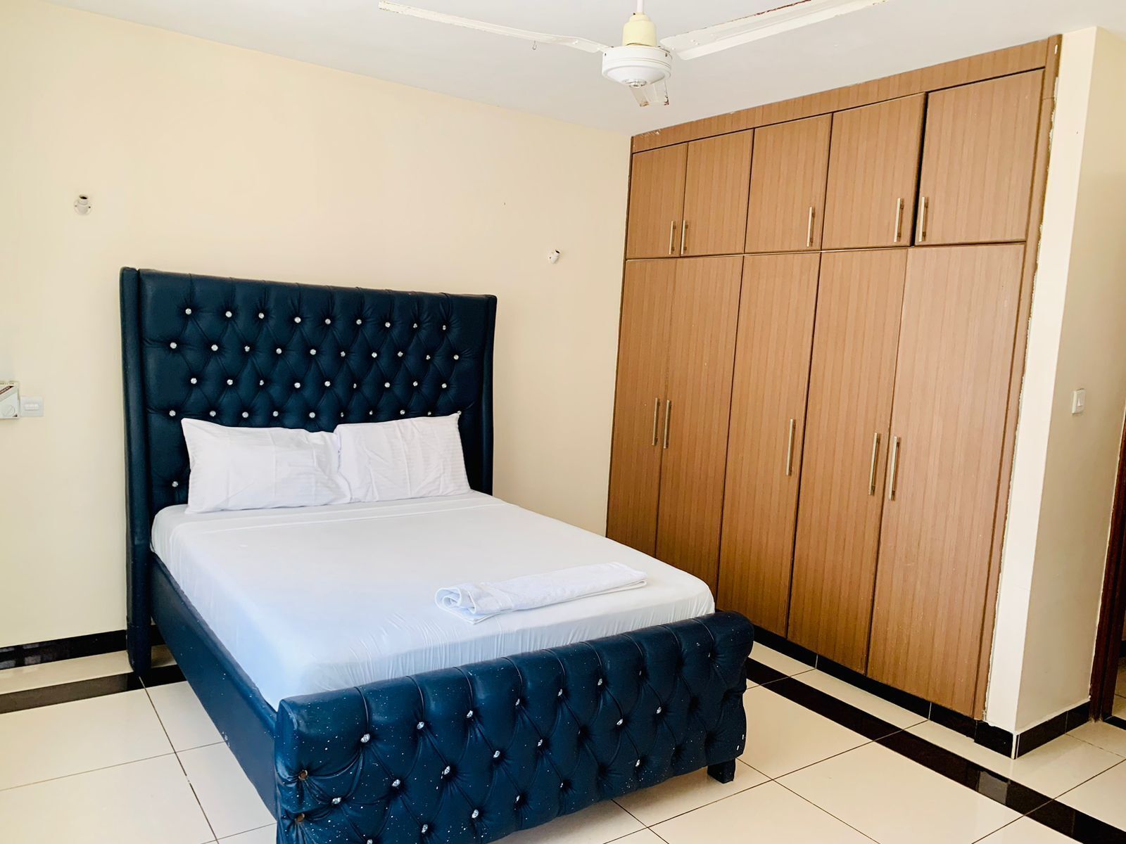 Un dormitorio con una cama tapizada azul oscuro, ropa de cama blanca y un armario de madera.