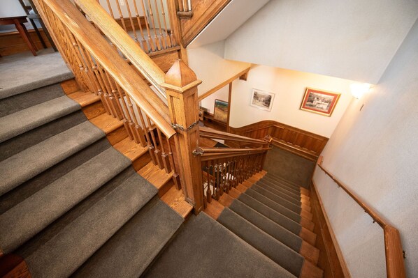 A wooden staircase with carpeted steps and a handrail, leading to a landing with a picture frame on the wall. - The Y On Broadway (Jim Thorpe)