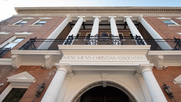 Fachada de edificio con una entrada amplia, columnas y un letrero que dice 'Young Men's Christian Association'.