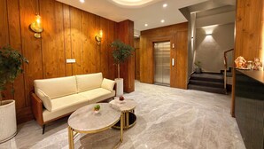 A modern lobby with a sofa, two round tables, wooden paneling, a staircase, and an elevator.