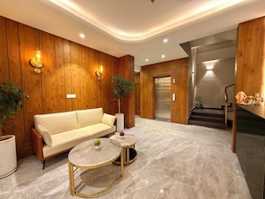 A modern lobby with a sofa, two round tables, wooden paneling, a staircase, and an elevator. - ARNISA Kasauli - A Boutique Hotel (Kasauli)
