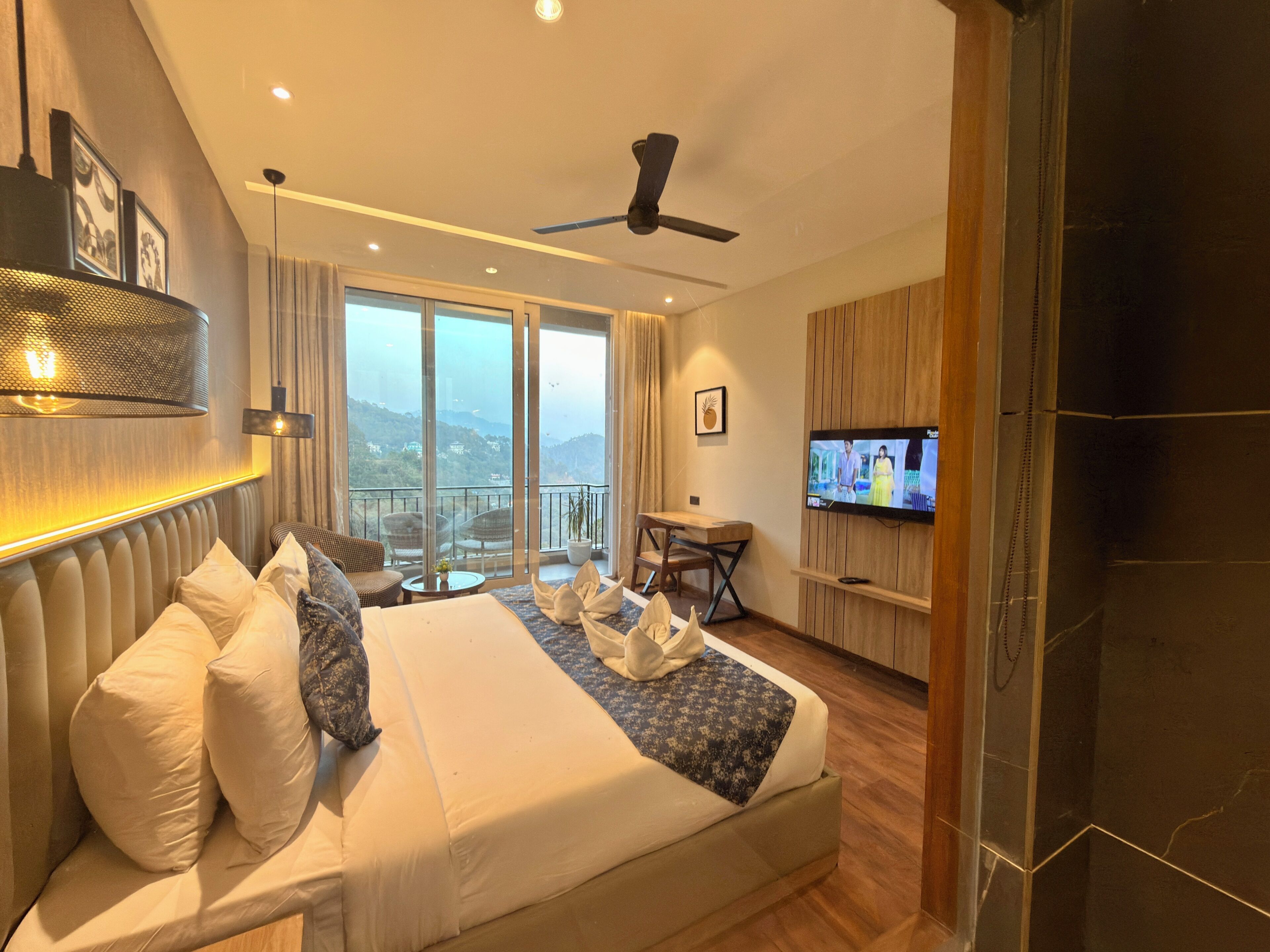 A hotel room with a bed, a TV, a balcony with a view, and a ceiling fan.