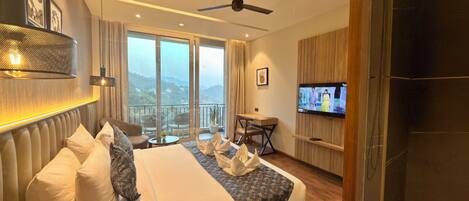 A hotel room with a bed, a TV, a balcony with a view, and a ceiling fan.