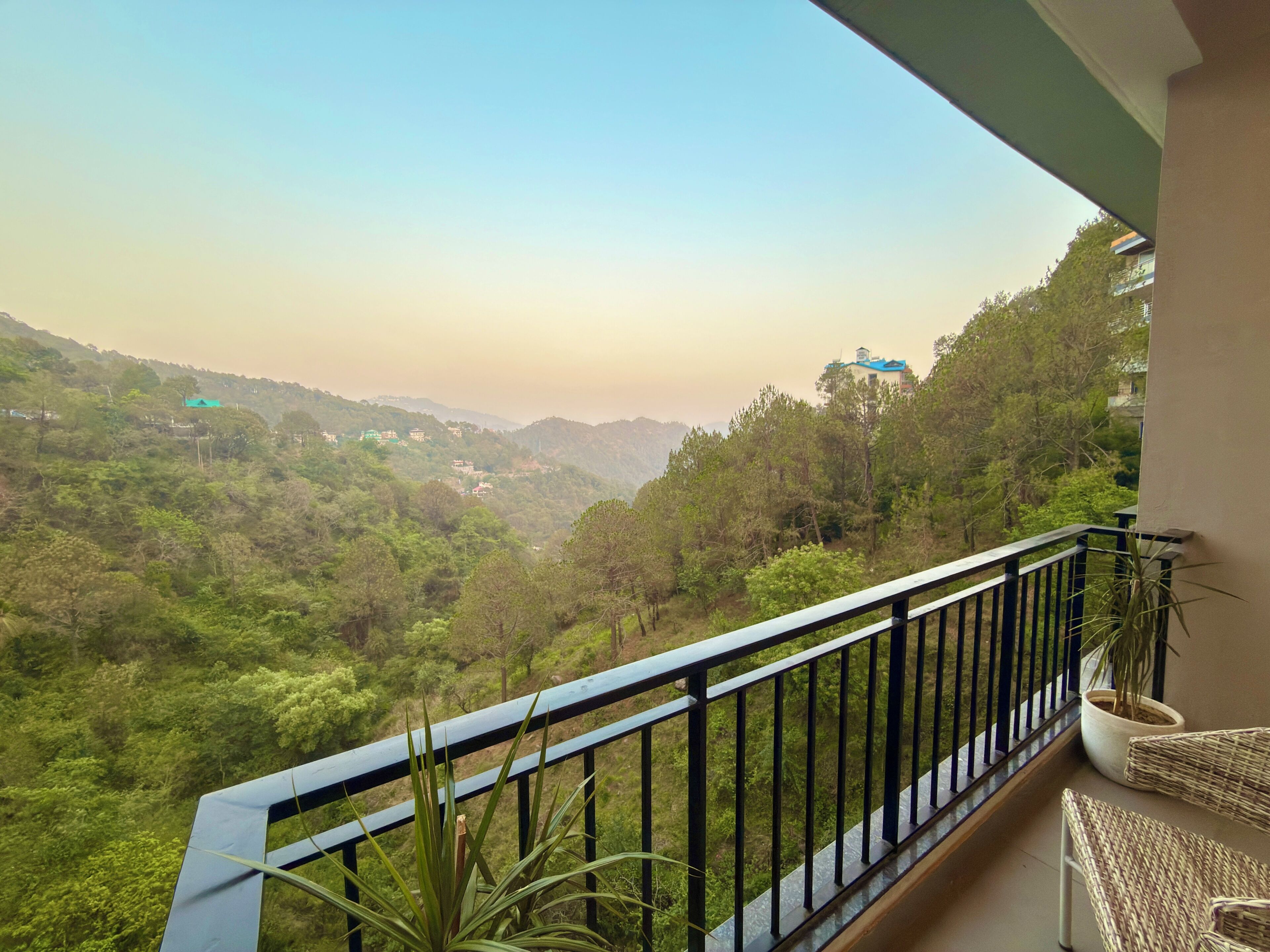 Ein Balkon mit Blick auf eine gebirgige Landschaft, einem Blumentopf und einem Korbstuhl.