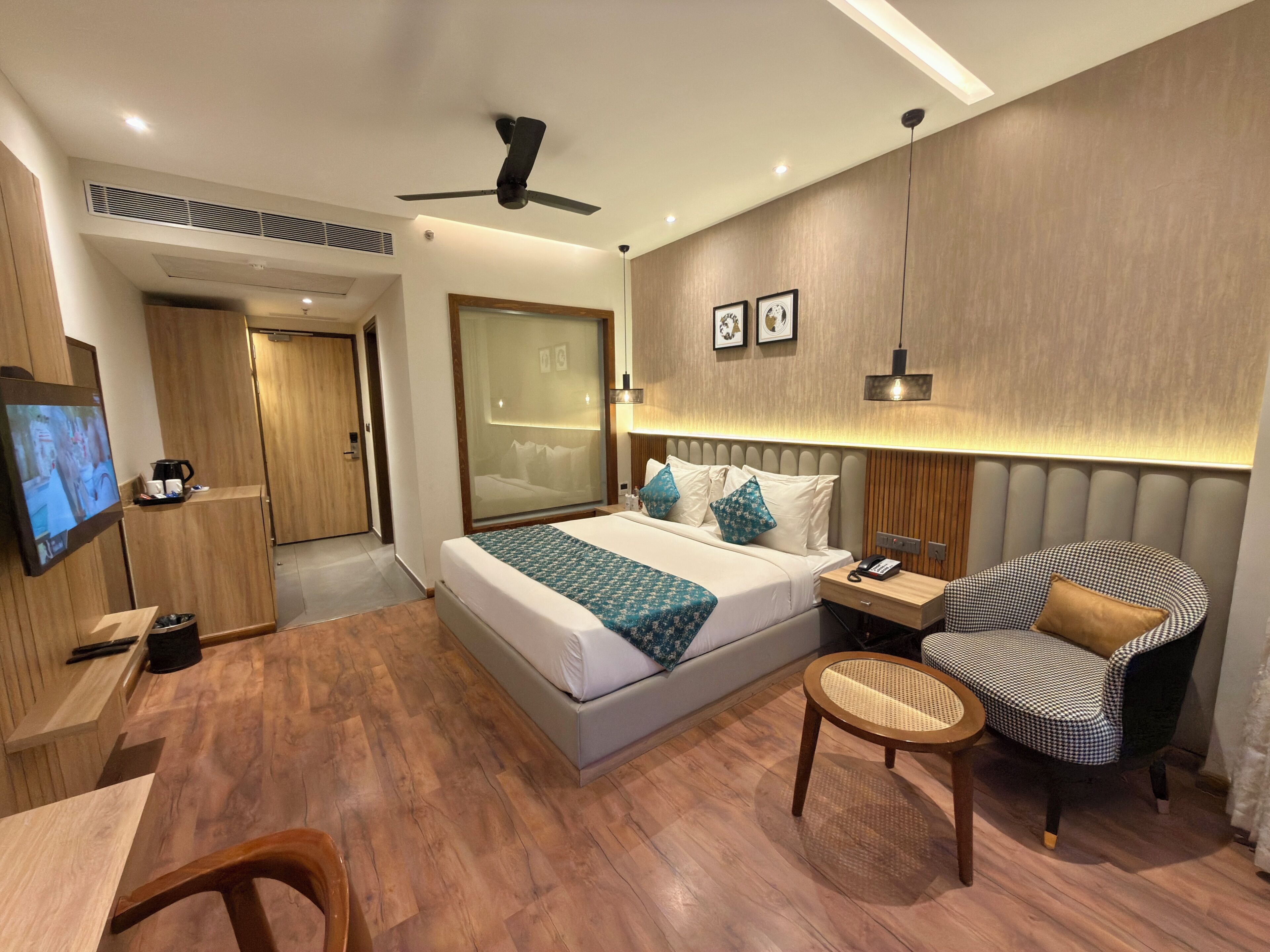 Una habitación de hotel moderna con cama, mesita de noche, silla, televisor y suelo de madera.