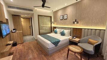 Una habitación de hotel moderna con cama, mesita de noche, silla, televisor y suelo de madera.