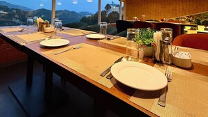 A dining area with a long table set for a meal, wooden ceiling, and large windows offering a view of the outdoors.