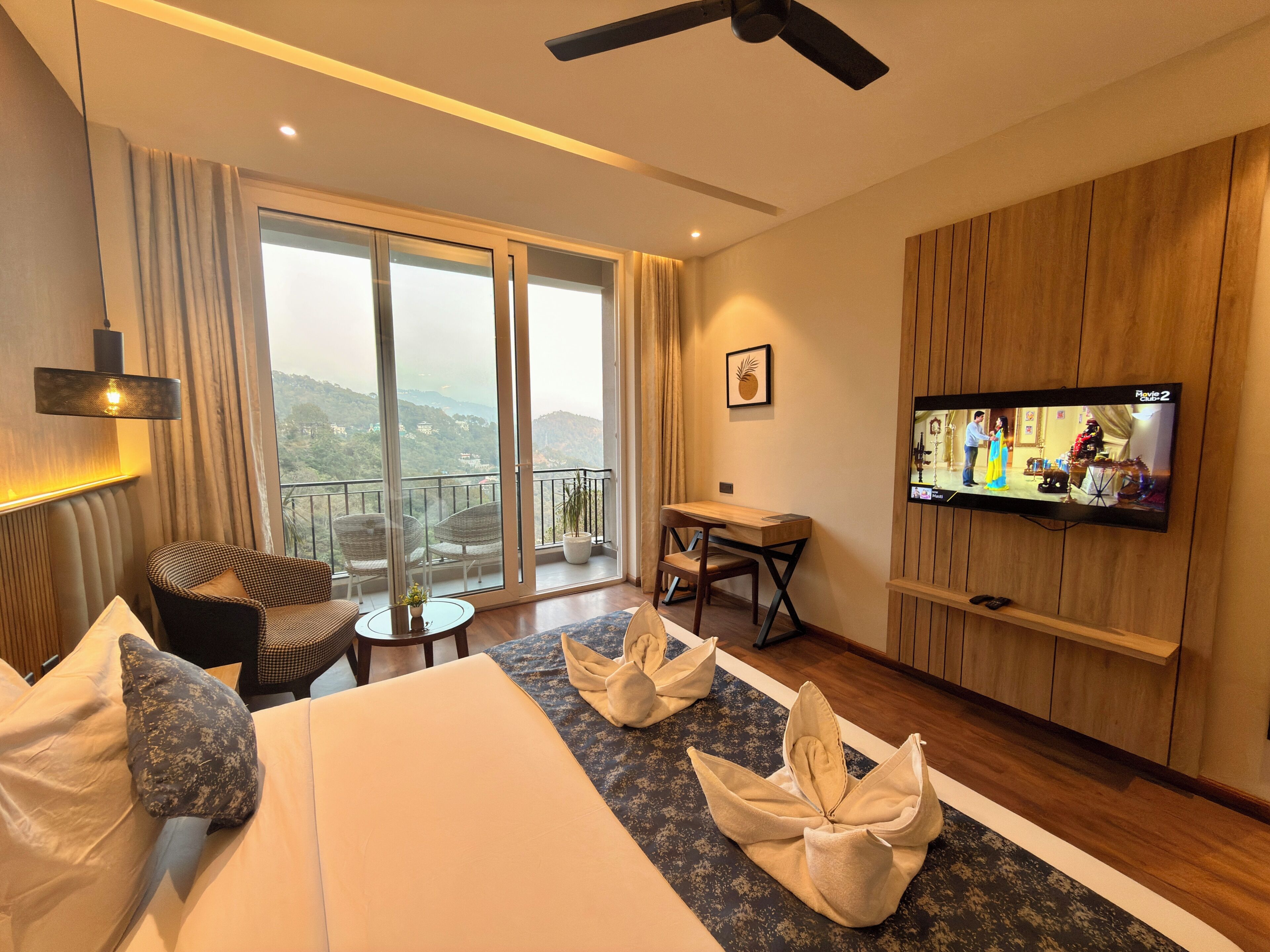 A hotel room with a bed, a desk, a television, and a balcony with a view.