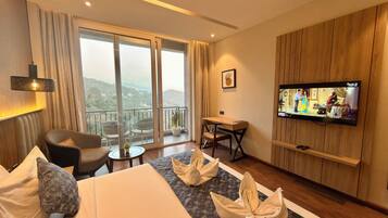 A hotel room with a bed, a desk, a television, and a balcony with a view.
