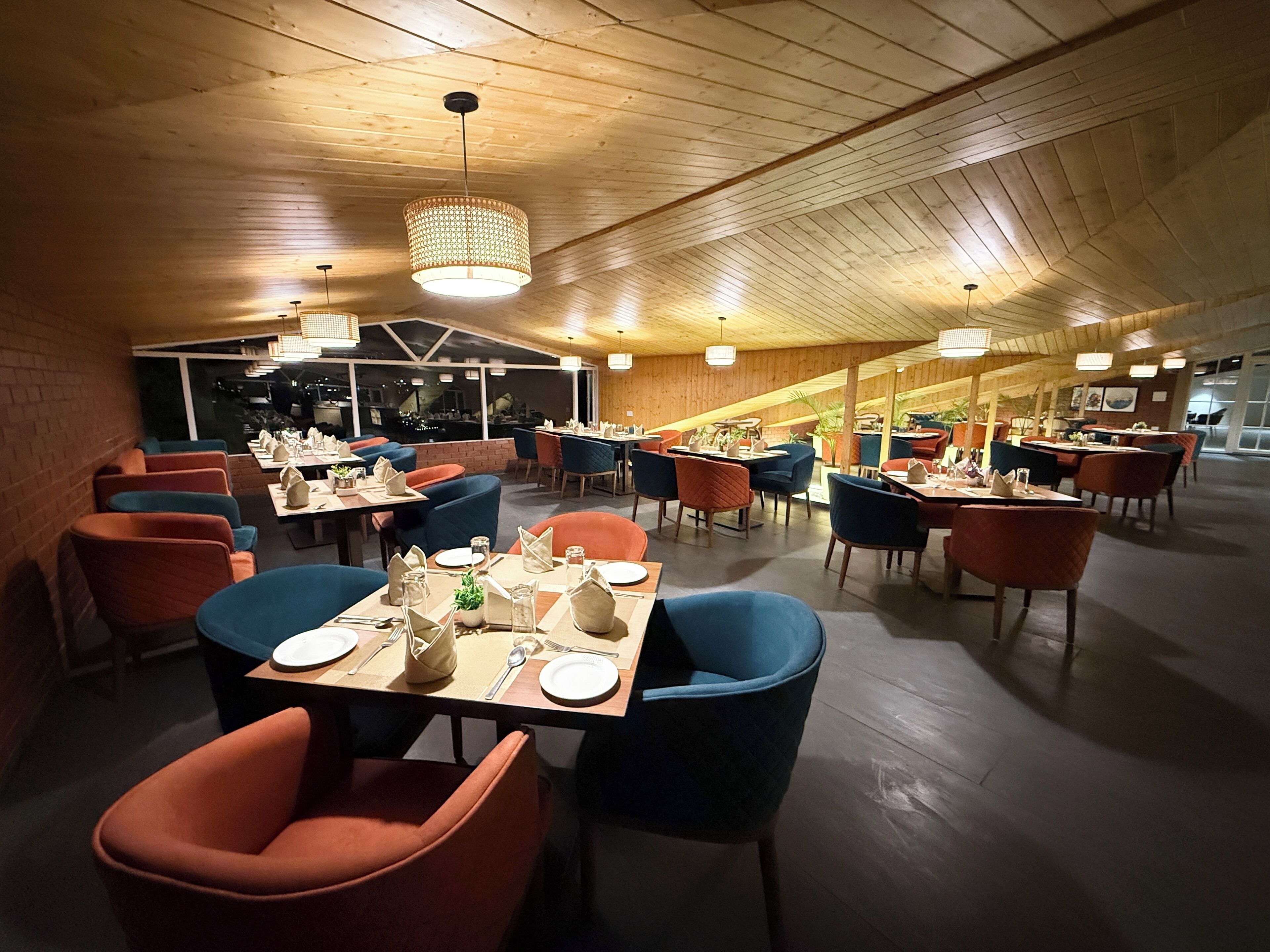 Un restaurant spacieux avec de hauts plafonds en bois et un mobilier moderne. Les tables sont dressées avec des assiettes, des couverts et des serviettes.
