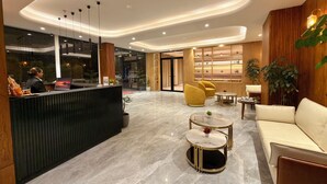 A modern hotel lobby with a reception desk, seating area, and a view of the outdoors.