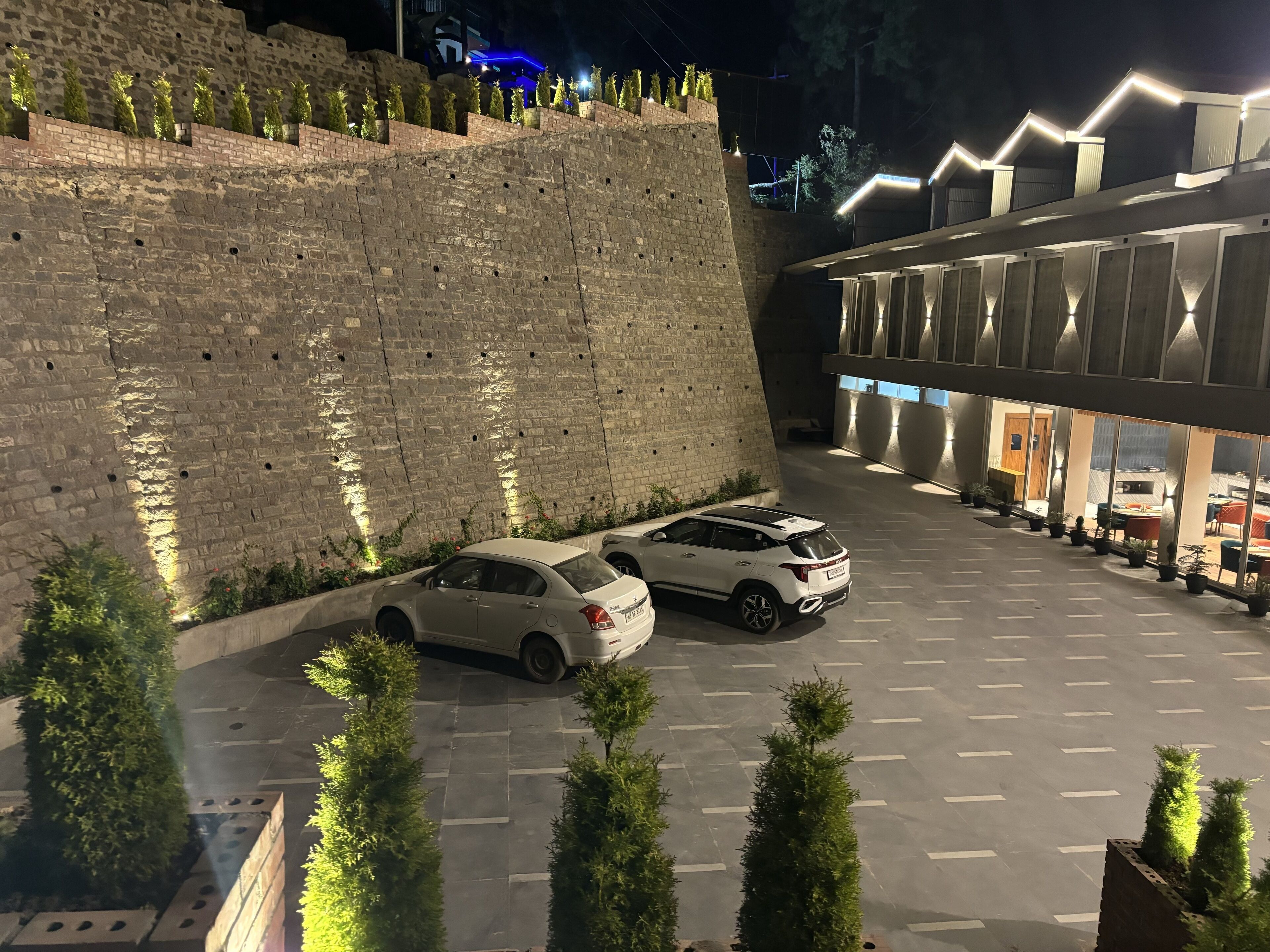 Uma área de estacionamento com dois carros, um muro de pedra e um edifício de arquitetura moderna.