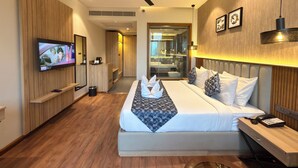 A modern hotel room with a large bed, a television, a ceiling fan, and a wooden floor.