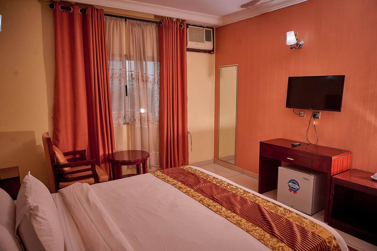 Een hotelkamer met een bed, een bureau, een stoel, een televisie en een minibar.