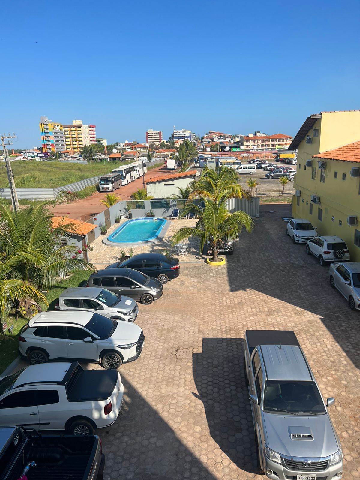 Un estacionamiento con varios coches, una piscina y edificios al fondo.