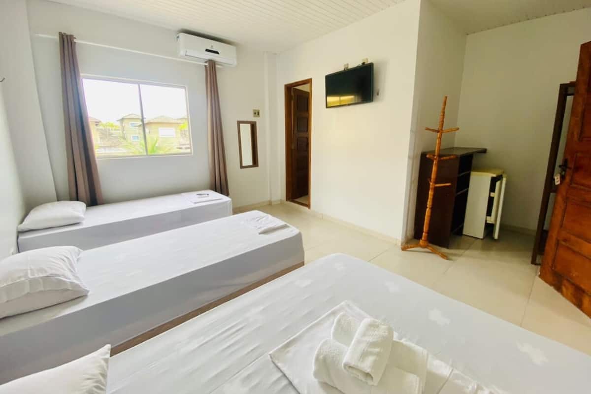A hotel room with two beds, a TV mounted on the wall, an air conditioning unit, and a view of the outside through the window.