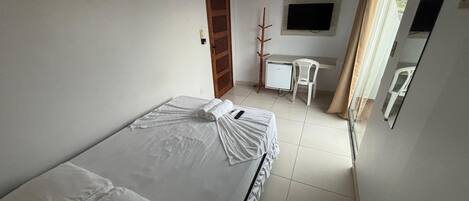 A small, clean room with a bed, a desk, a chair, a TV, and a window with curtains.