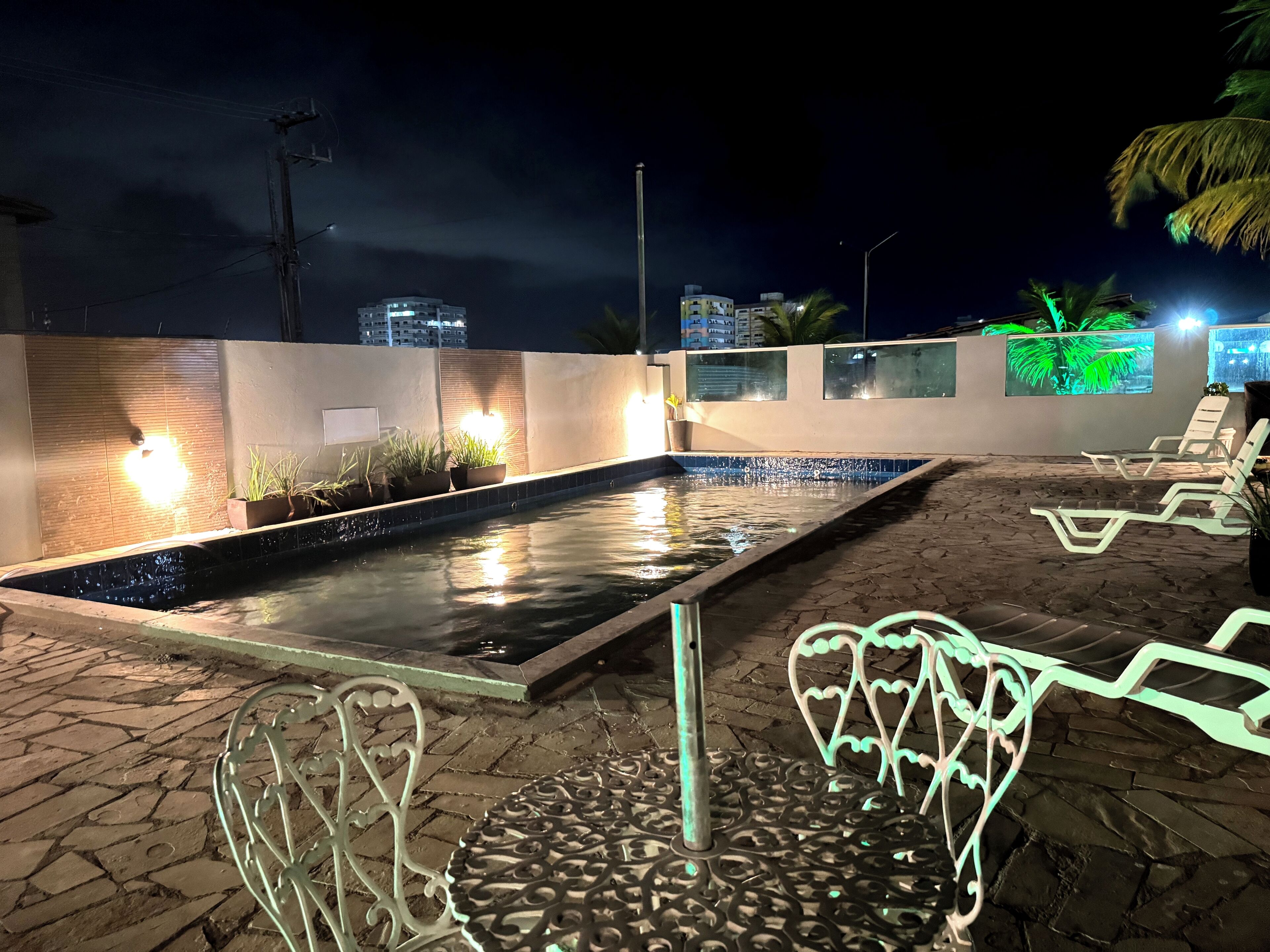 A nighttime outdoor pool area with lounge chairs and potted plants.