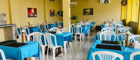 A restaurant with multiple tables covered in blue tablecloths, white chairs, and hanging black pendant lights.