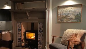 A cozy living room with a fireplace, a comfortable armchair, and a painting on the wall.