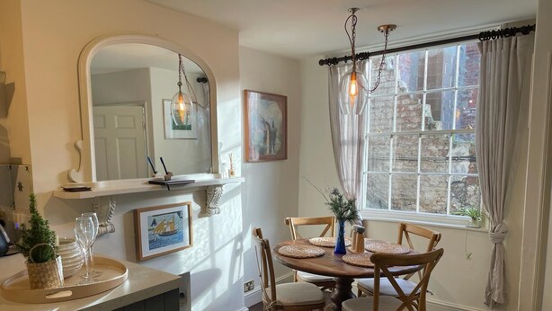A dining area with a round wooden table, six chairs, a mirror, and a window with curtains.