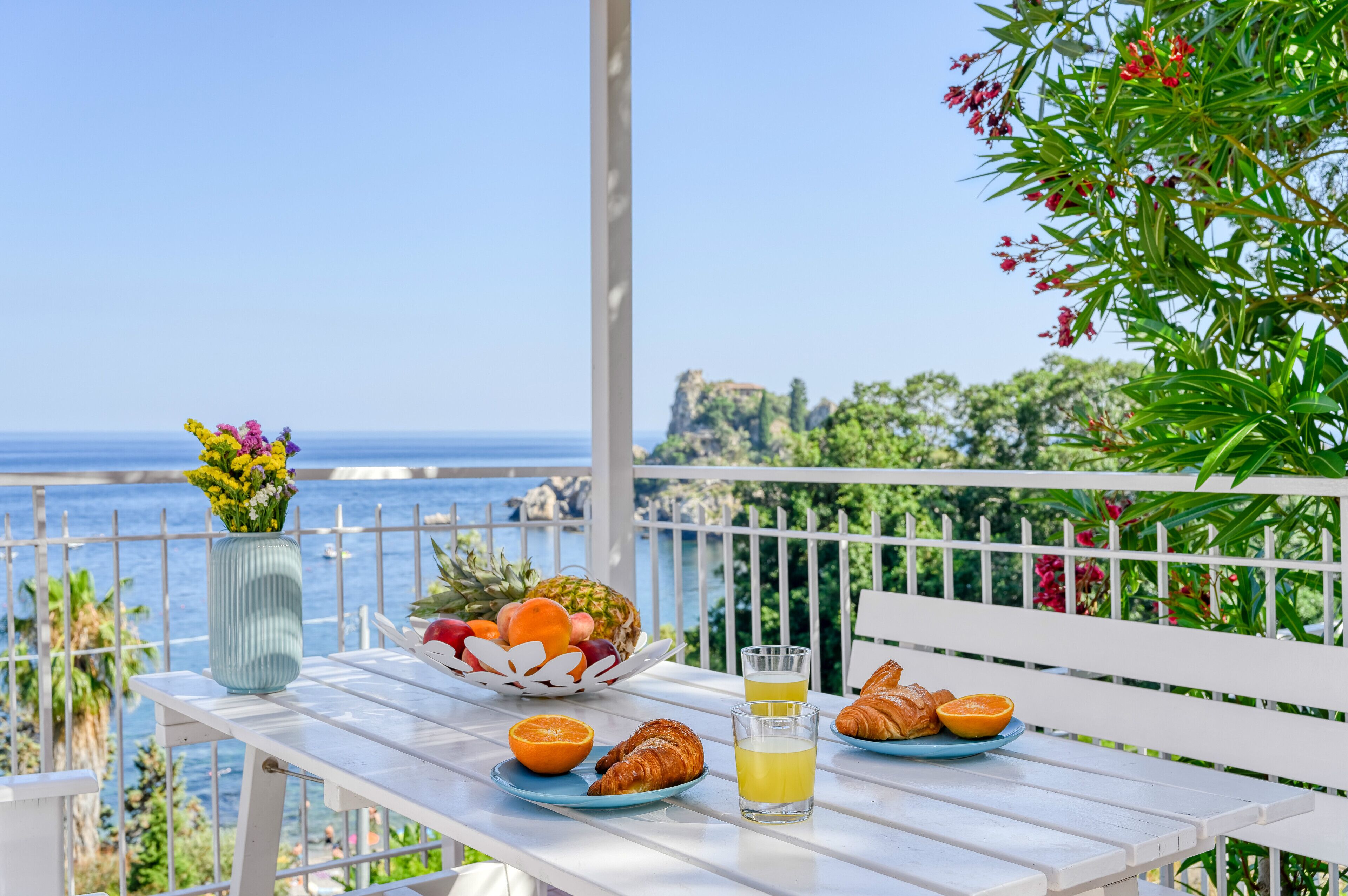 Una mesa con alimentos para el desayuno, un jarrón de flores y vista al mar.