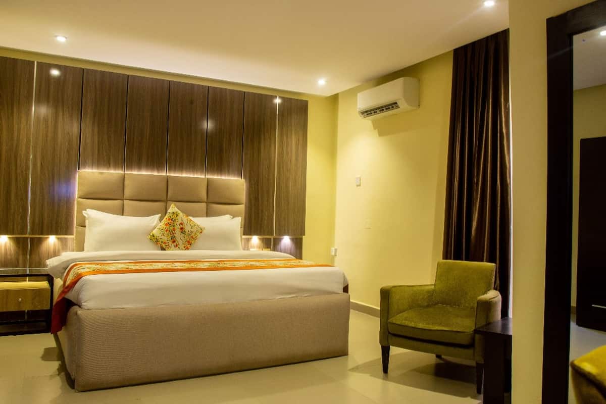 A modern hotel room with a large bed, a green armchair, and a built-in wardrobe.