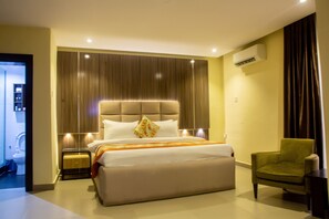 Habitació d'hotel moderna amb un llit gran, un butaca verda i un panell de capçal integrat.