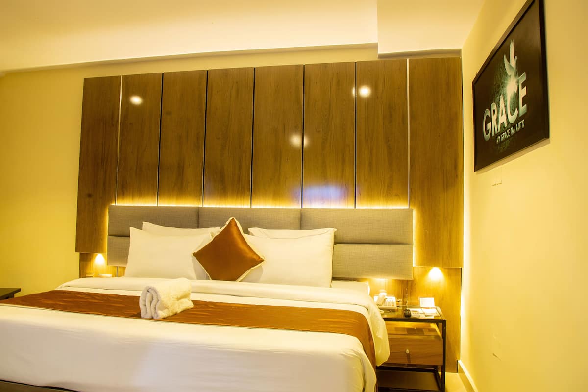 A hotel room with a large bed, wooden headboard, and a framed 'GRACE' sign on the wall.
