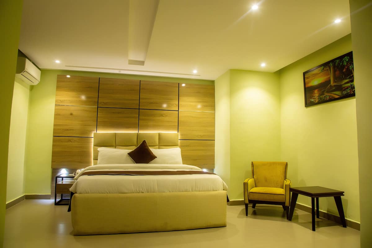 A modern bedroom with a large bed, a headboard with built-in lighting, a bedside table, a chair, and a small table.
