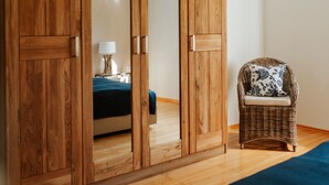 Une chambre avec une armoire en bois, une chaise en osier et un lit recouvert d’une couverture bleue.