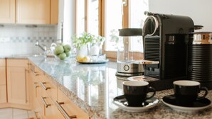 Une cuisine équipée d’une machine à café, de deux tasses et d’un panier de fruits.