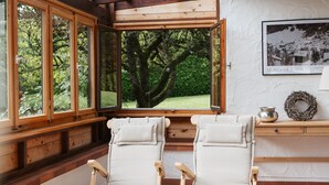 Une pièce comprenant deux fauteuils inclinables, un banc en bois, une petite table avec un pot en métal et une couronne, ainsi qu’un tableau encadré accroché au mur.